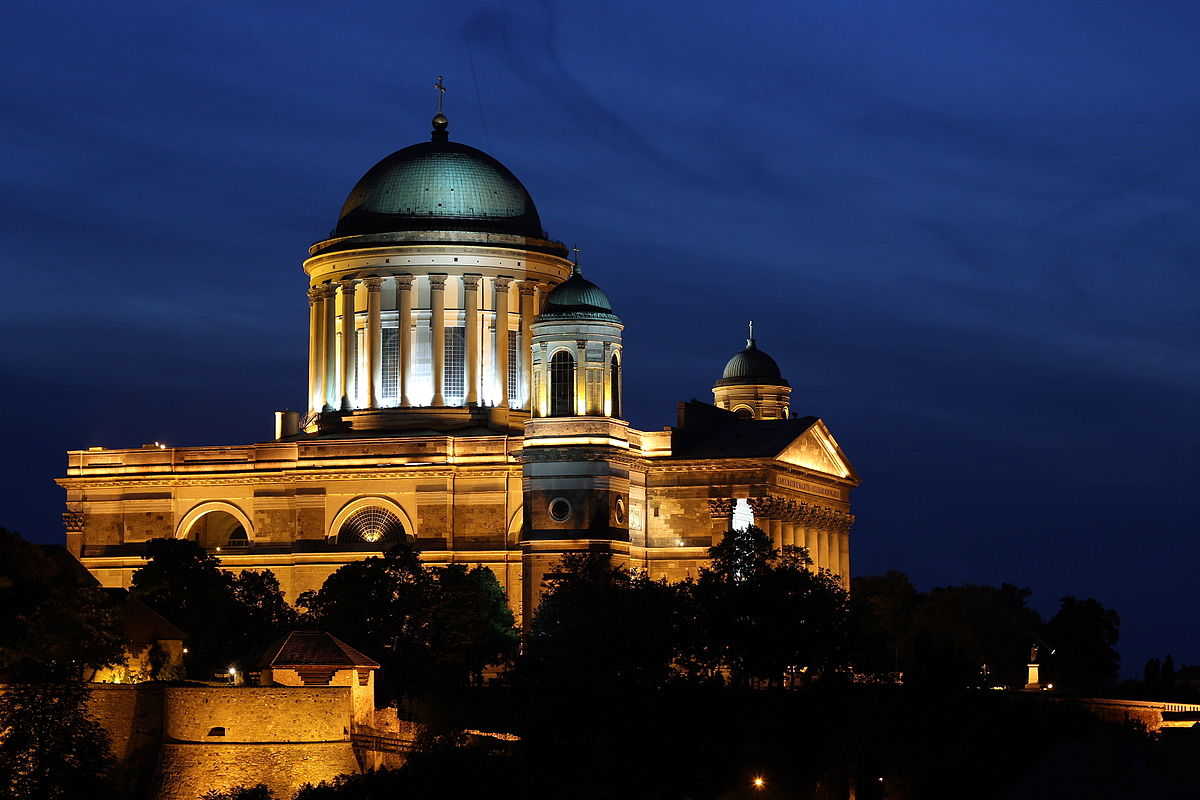 A bazilika éjszakai kivilágításban a Szent Tamás-hegyről nézve, előtérben az esztergomi vár Budai kapuja